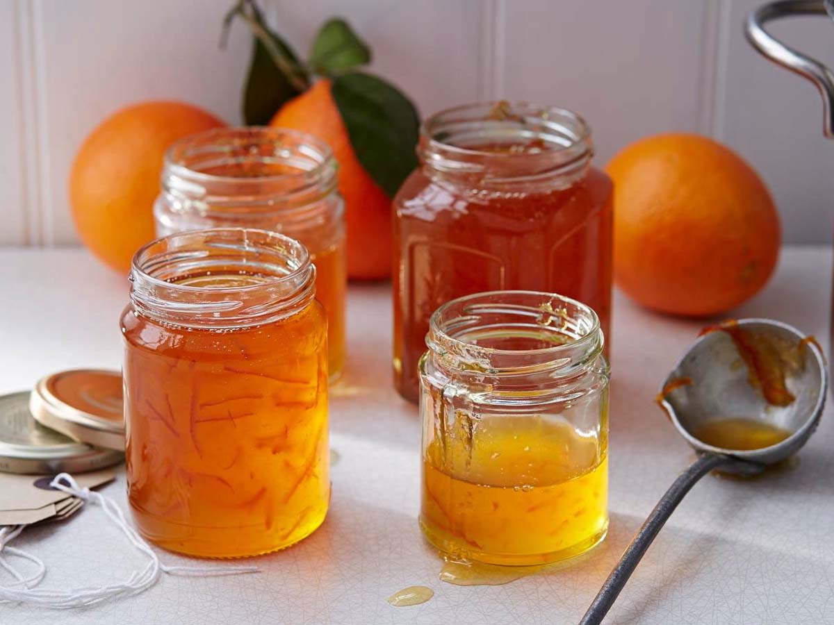 A jar of thick, glassy bitter sweet Seville orange marmalade jam showing citrus rinds.